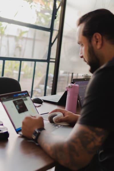 Man working on a laptop with a pink water bottle nearby